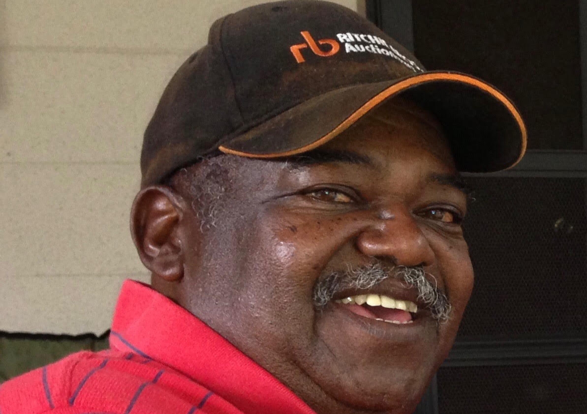 A photograph of Lump Boston. He is wearing a black hat and a red shirt with black stripes.
